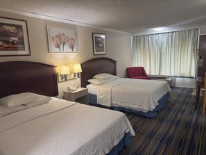 A hotel room with two beds, a red chair, a nightstand with a phone, and a window with curtains. - Wagner Inn (Eureka Springs)