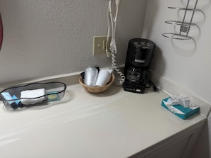 A kitchenette with a coffee maker, a basket with toiletries, a tissue box, and a power outlet. - Wagner Inn (Eureka Springs)