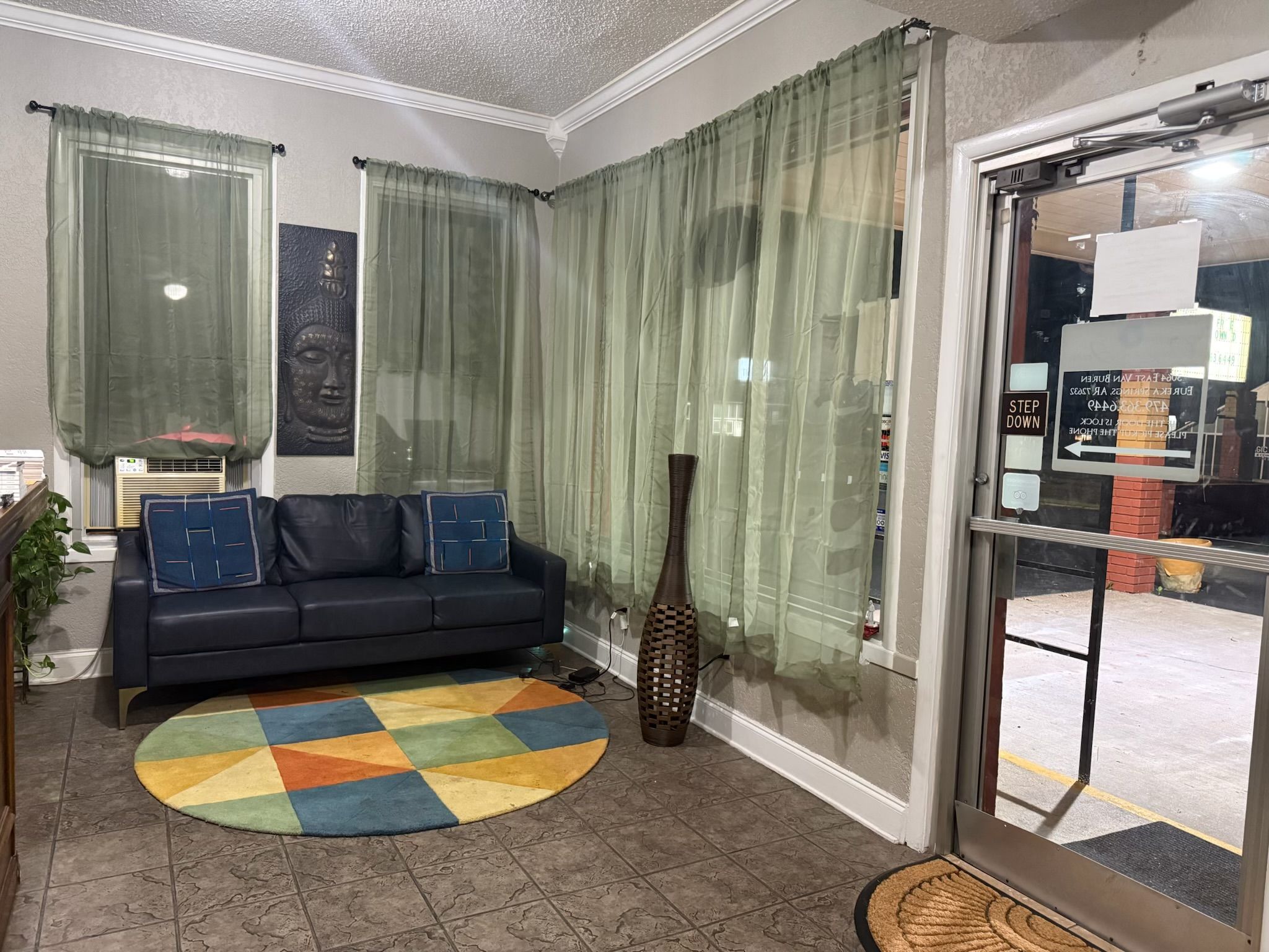 A living room with a black sofa, a colorful rug, a tall vase, and sheer curtains.