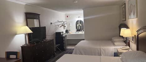 Habitación de hotel con dos camas, un escritorio, un televisor, un aparador, un espejo, un tocador con lavabo y un teléfono.