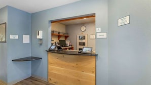 Zona de recepción con mostrador de madera, un reloj y un cartel que indica los horarios de registro de entrada y salida.