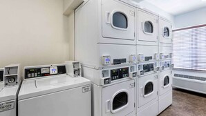 Un área de lavandería con varias lavadoras y secadoras apiladas, cada una con pantallas digitales y paneles de control.