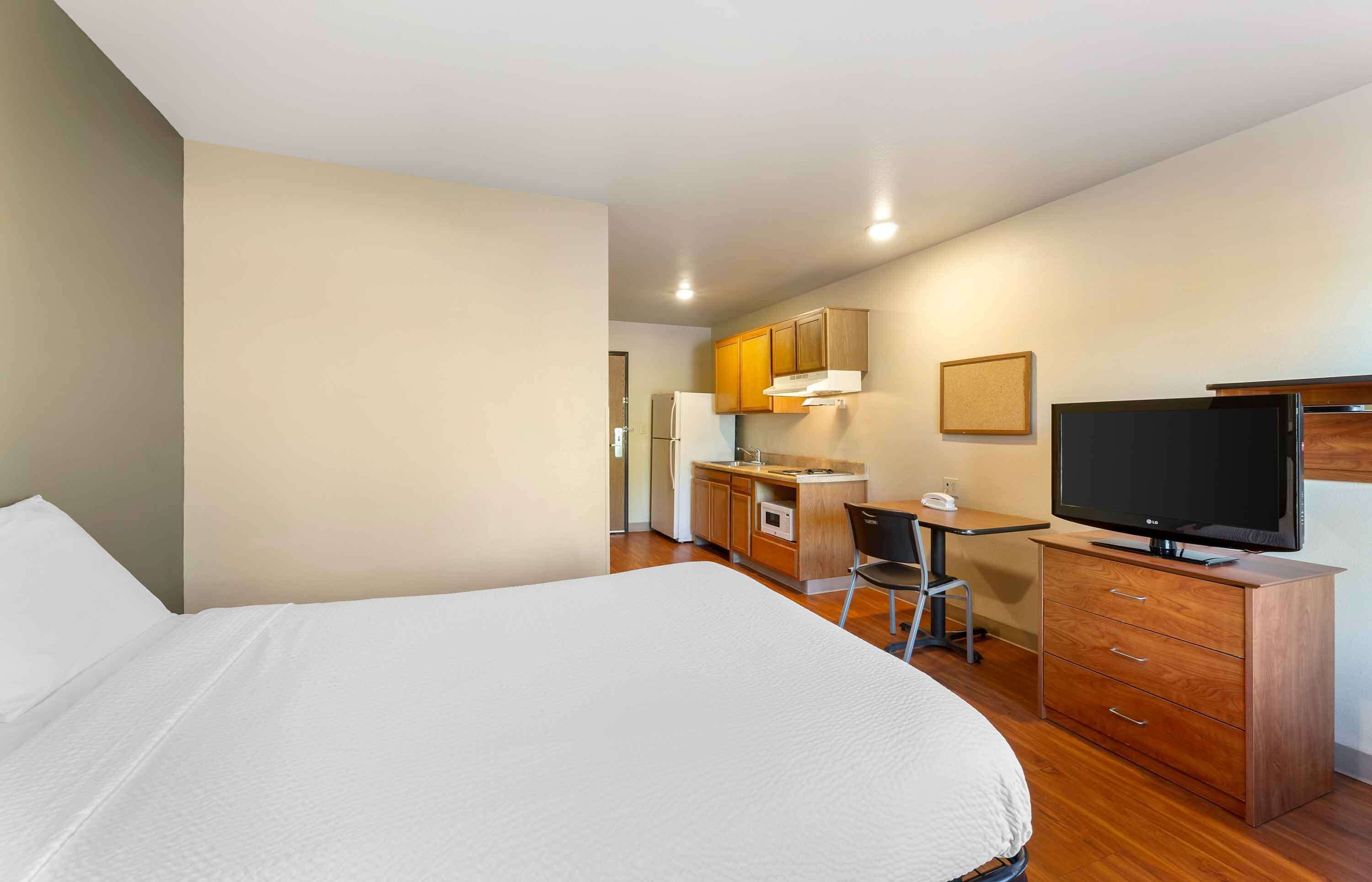 Quarto de hotel com uma cama grande, uma escrivaninha com cadeira, televisão e armários de madeira.