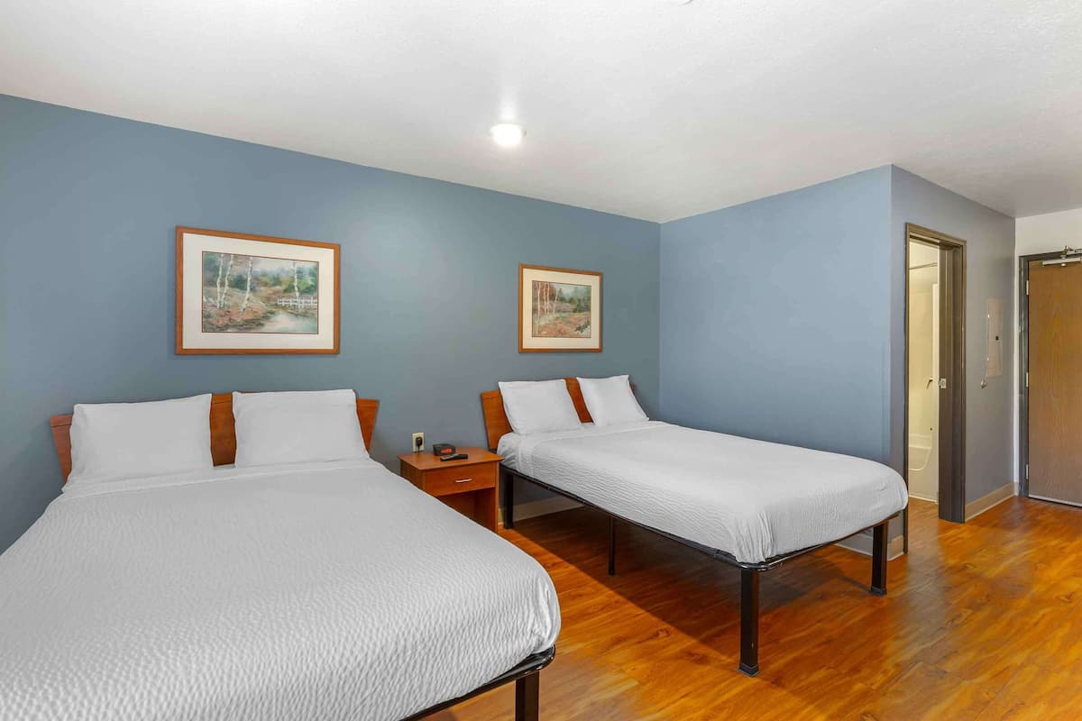 A room with two single beds, wooden headboards, a nightstand with a lamp, and two framed pictures on the wall.