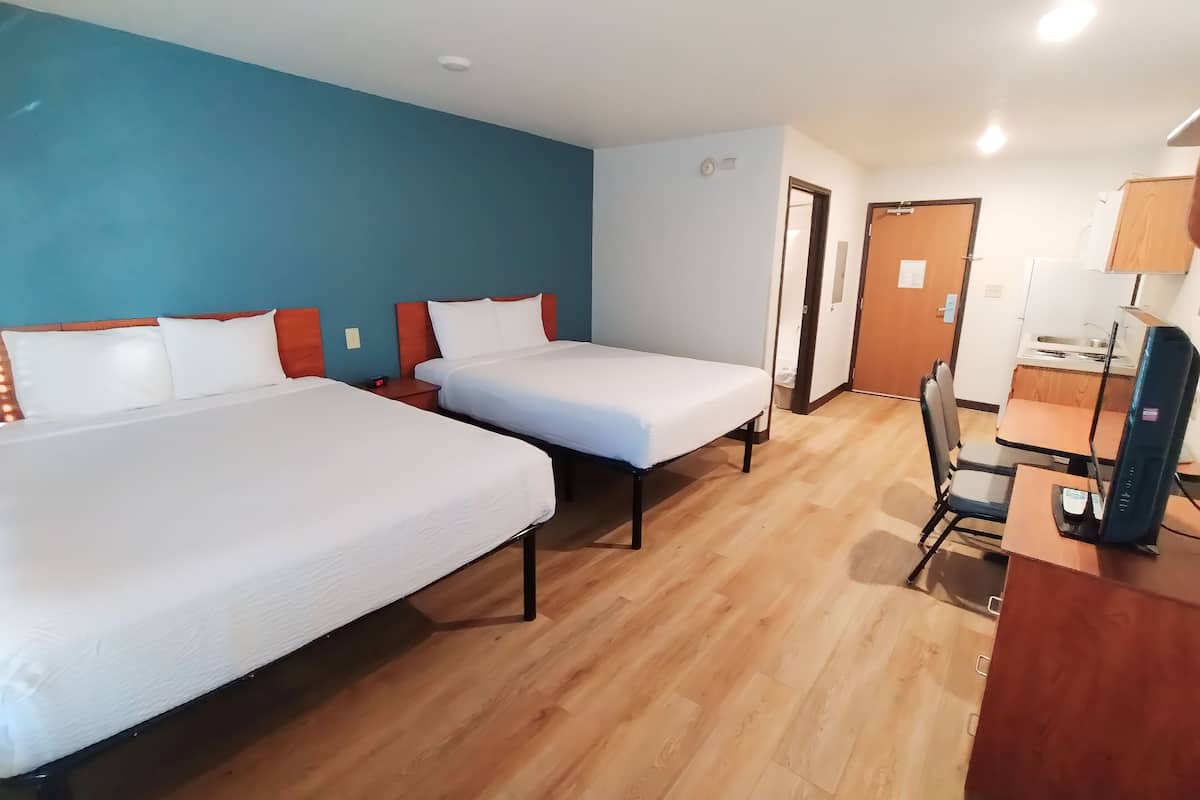 A hotel room with two beds, a desk, and a chair.