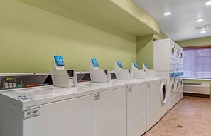 A laundry facility with multiple washing machines and dryers, a control panel, and a window with blinds. - Extended Stay America Select Suites - Indianapolis - Greenwood (Greenwood)