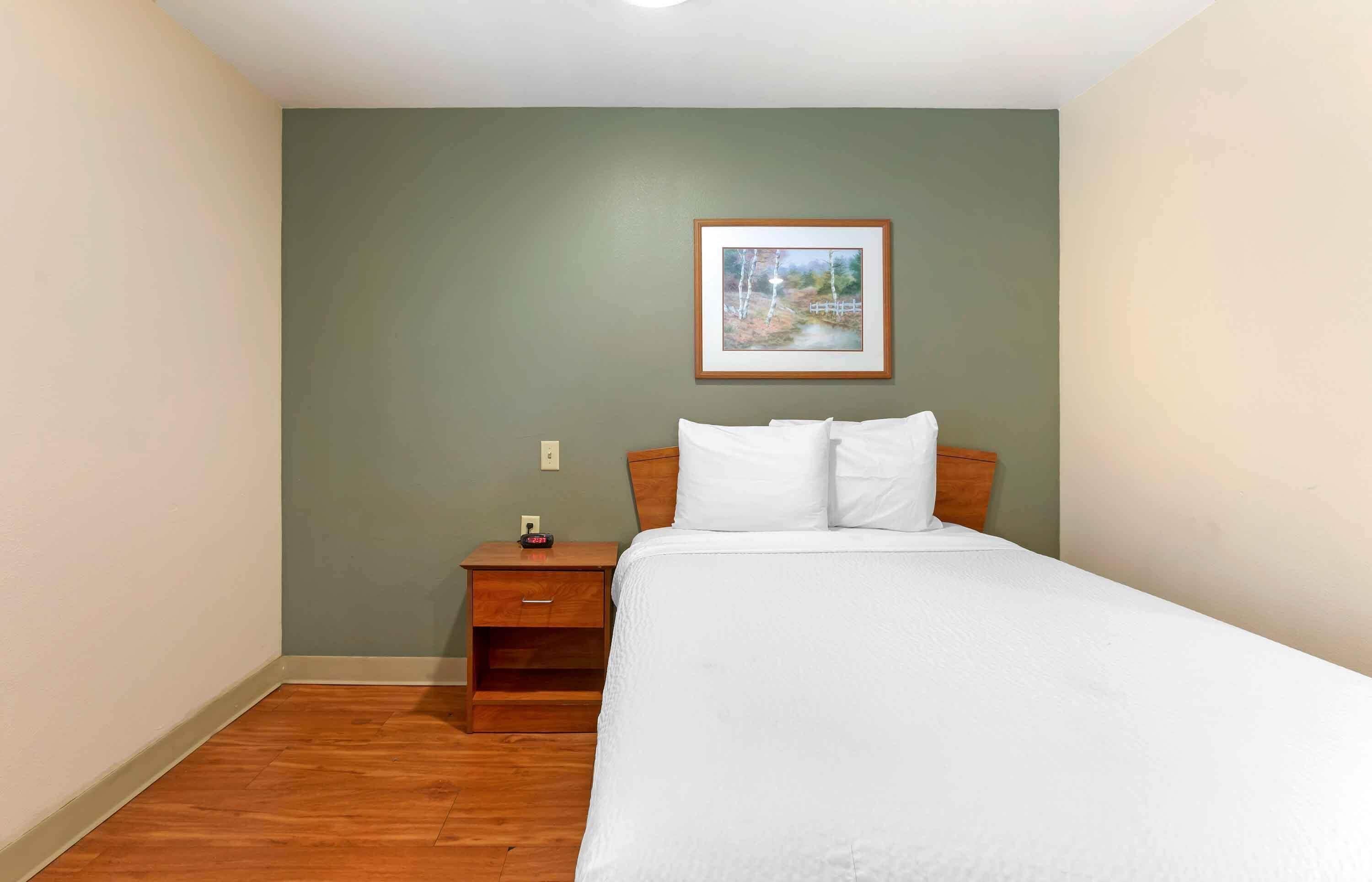 Habitación de hotel con cama, mesita de noche, un cuadro enmarcado en la pared y piso de madera.