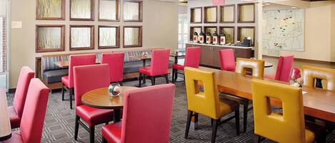 A hotel lobby with red and yellow chairs, a wooden table, and framed artwork on the walls.