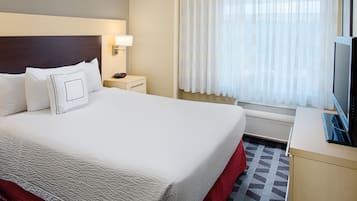 A hotel room with a large bed, a bedside table with a lamp, a TV, and a window with sheer curtains.