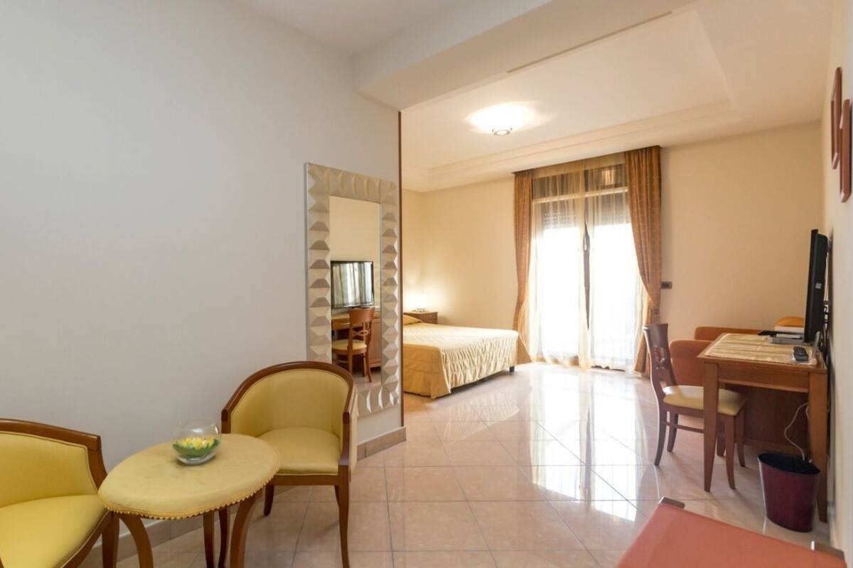 A hotel room with a bed, a desk, two chairs, a small table, and a mirror.