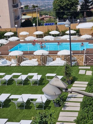 Une piscine dotée de chaises longues et de parasols, entourée d’une pelouse et offrant une vue sur le paysage urbain.