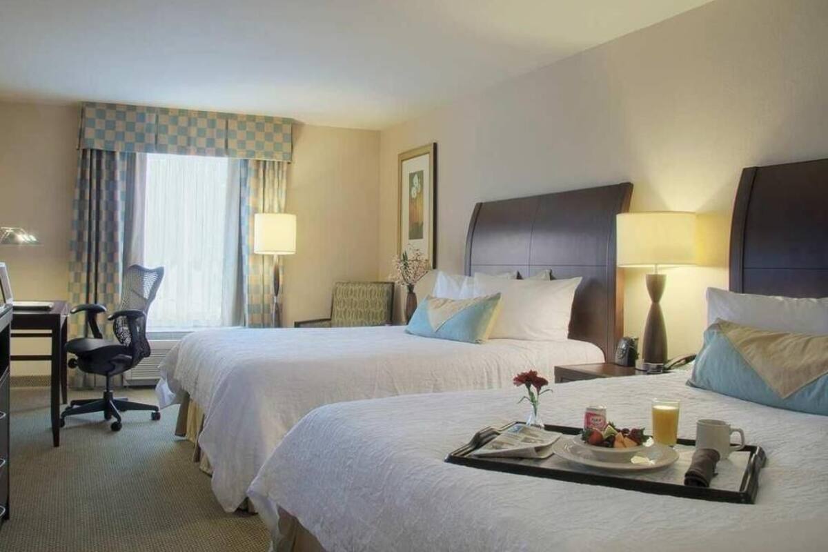 A hotel room with two beds, a desk, a chair, and a tray with breakfast items.