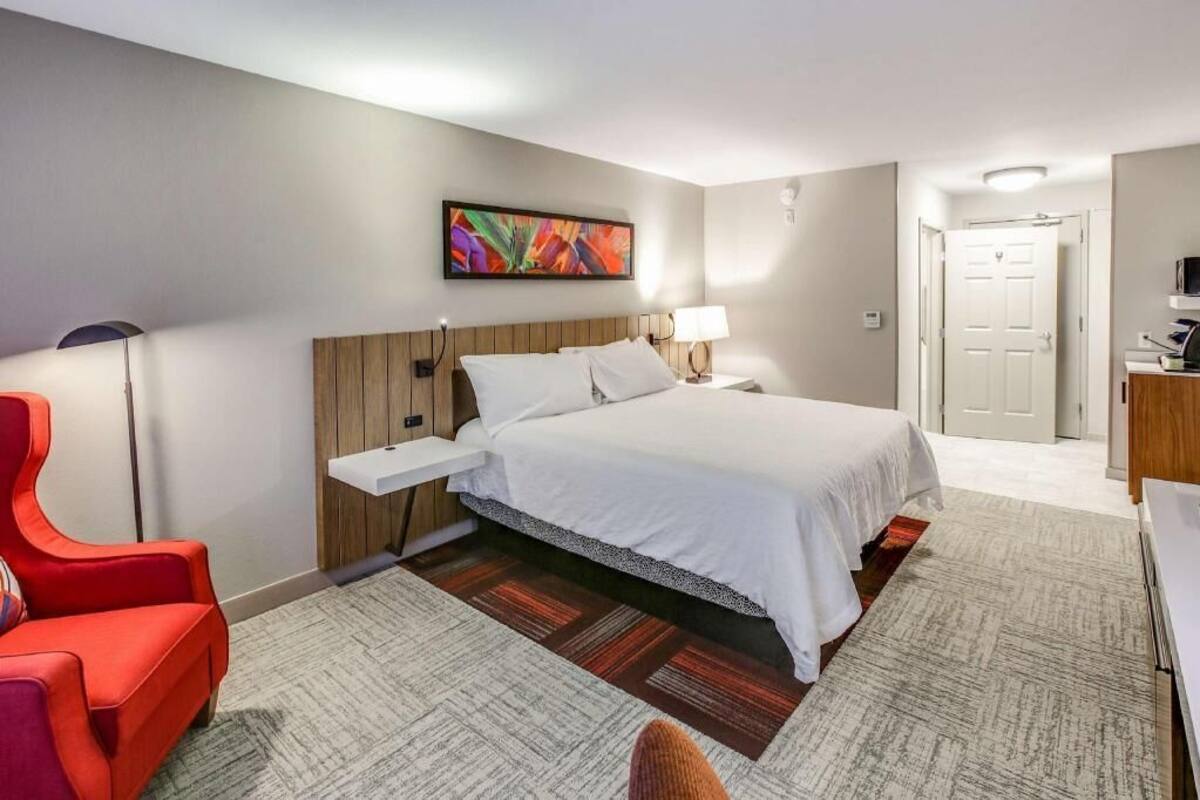 A hotel room with a bed, a nightstand, a red chair, a desk, and a television.