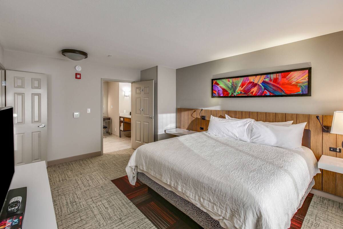 A hotel room with a large bed, a flat-screen TV, a desk, and a painting on the wall.