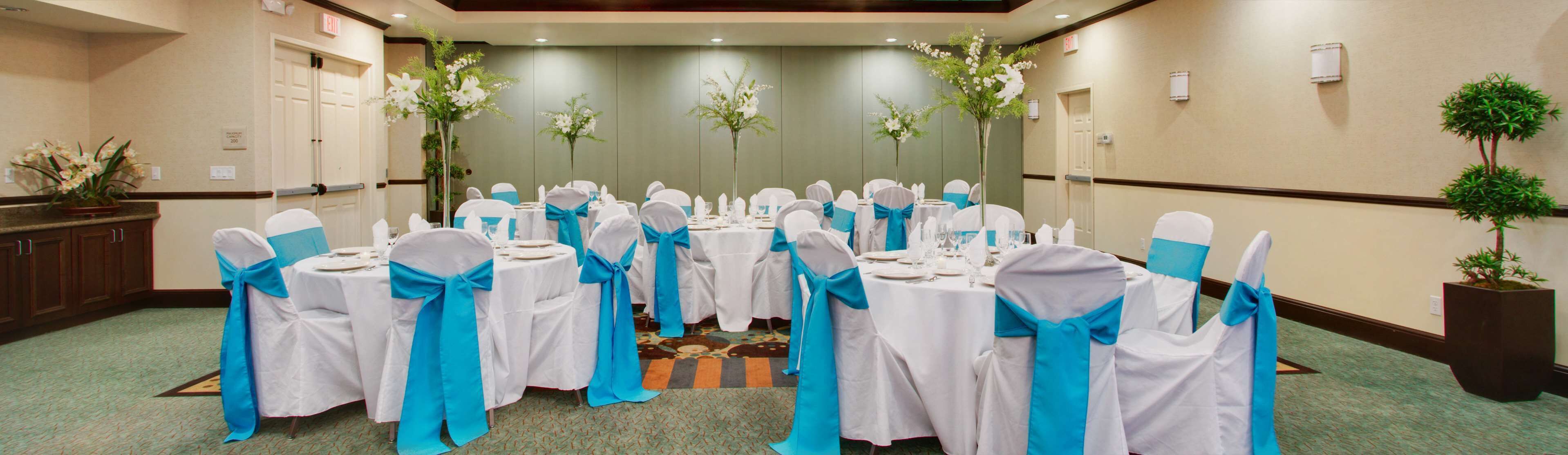 Une salle de conférence avec des tables rondes, des nappes blanches et des chaises ornées de rubans bleus.