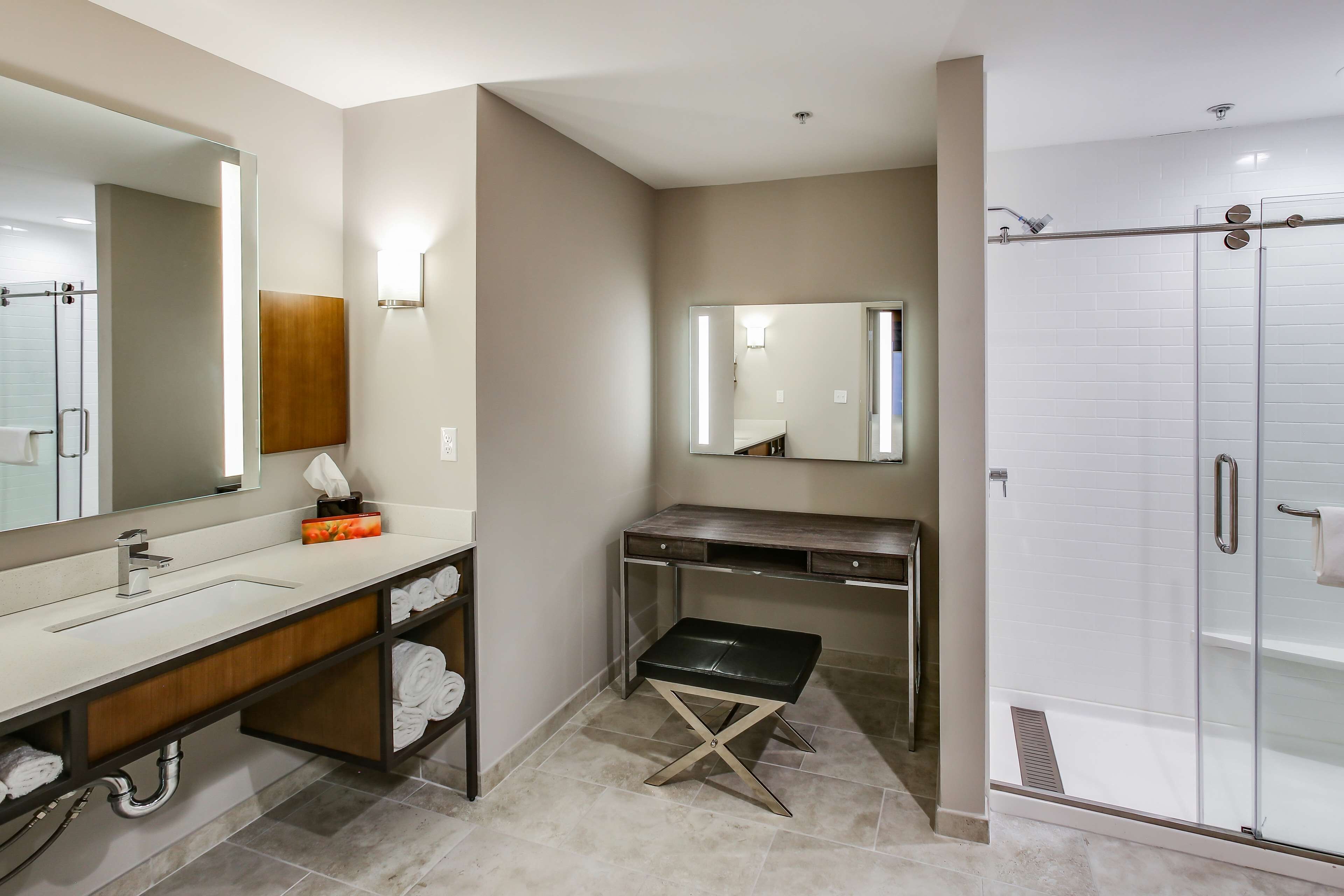 A modern bathroom with a large mirror, a vanity with a sink, a shower enclosure, and a bench.