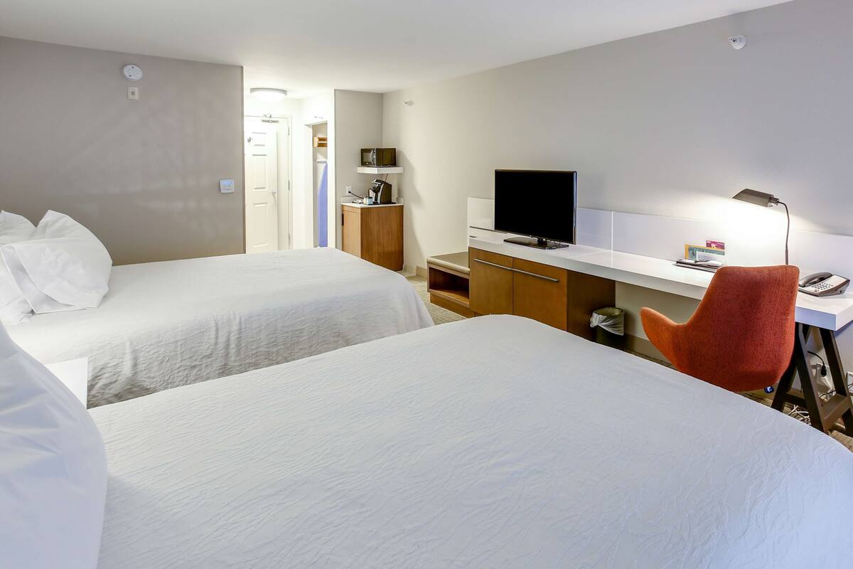 A hotel room with two beds, a desk with a TV, a lamp, and a red chair.
