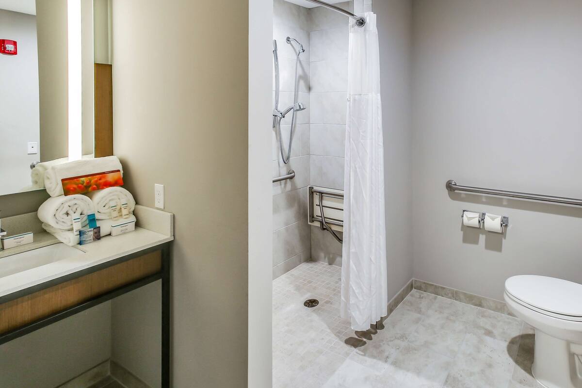 A bathroom with a shower, toilet, and a towel rack with towels.