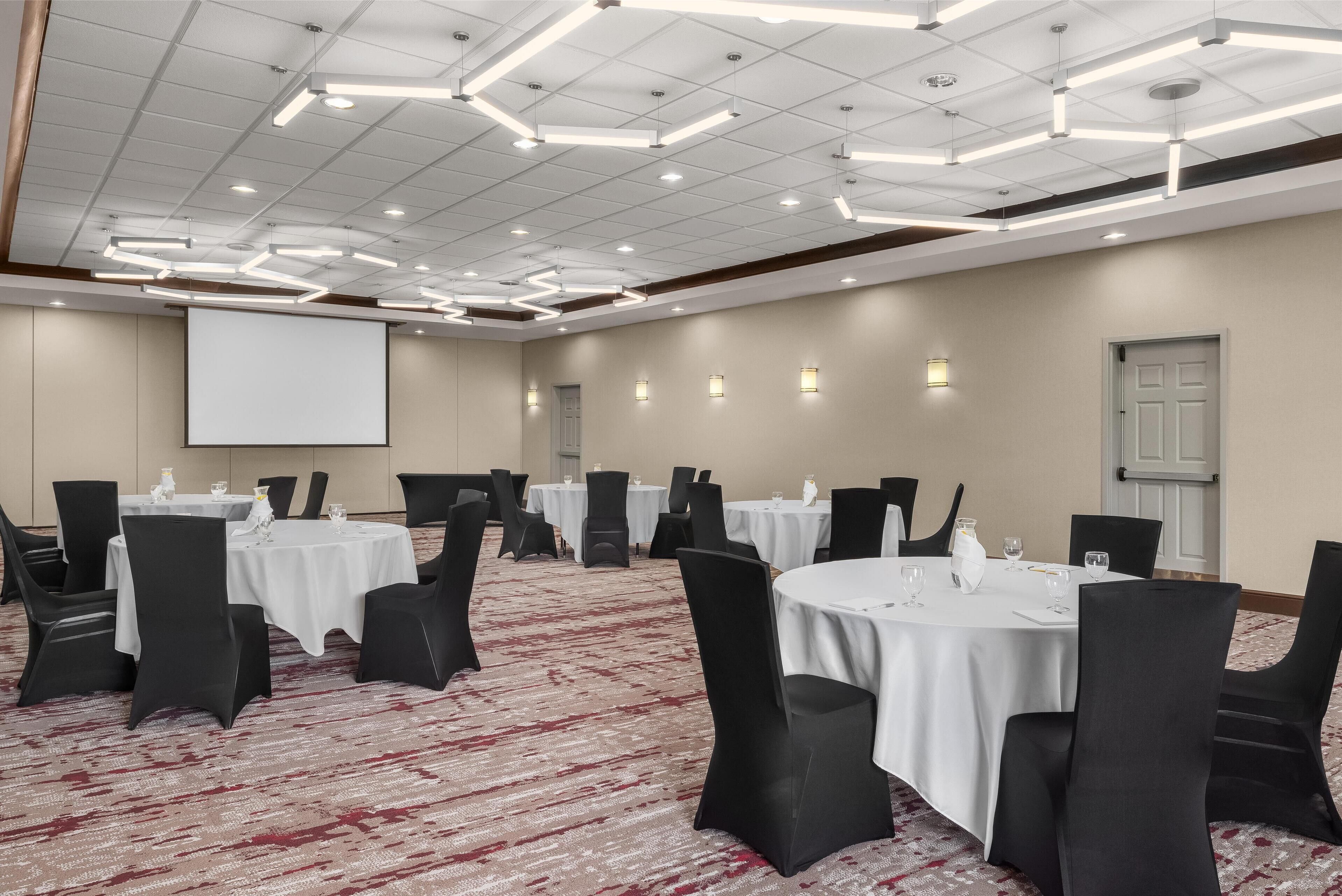 A conference room with round tables, black chairs, and a projector screen.