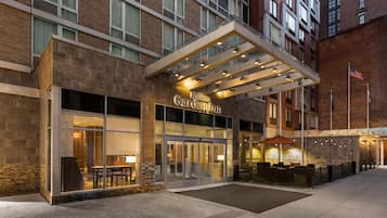 A hotel entrance with a glass facade, outdoor seating area, and a flag.