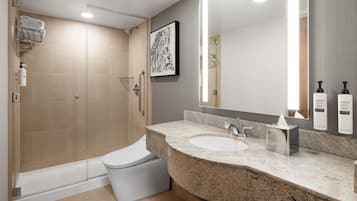 Et moderne badeværelse med en glasafskærmet brusekabine, et hvidt toilet, en vask med granitbordplade og et stort spejl.