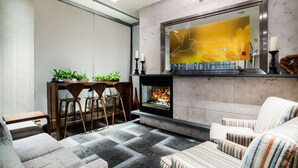 Un salon moderne doté d’une cheminée, de fauteuils à rayures, d’un coin repas avec des chaises et une table, ainsi qu’une grande œuvre d’art accrochée au mur.