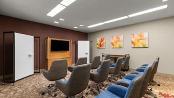 A conference room with a flat-screen TV, multiple chairs, and three floral paintings on the wall.
