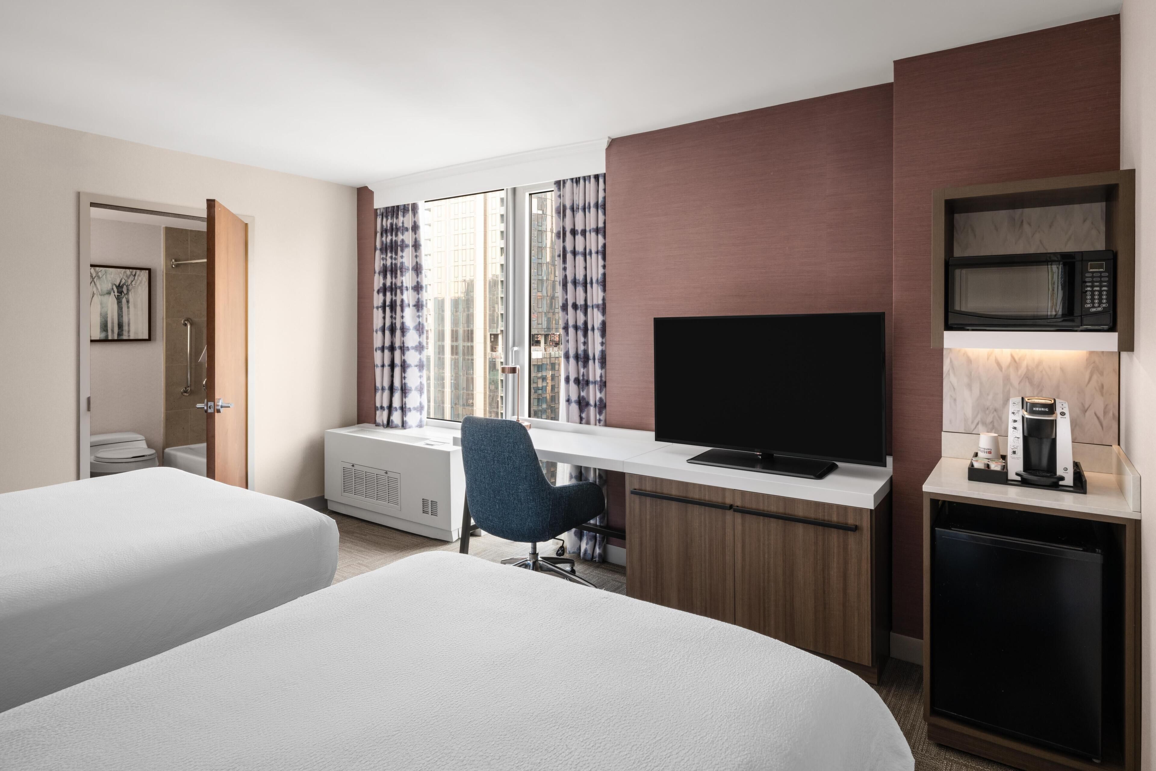 A hotel room with two beds, a desk with a TV, a coffee maker, and a microwave.