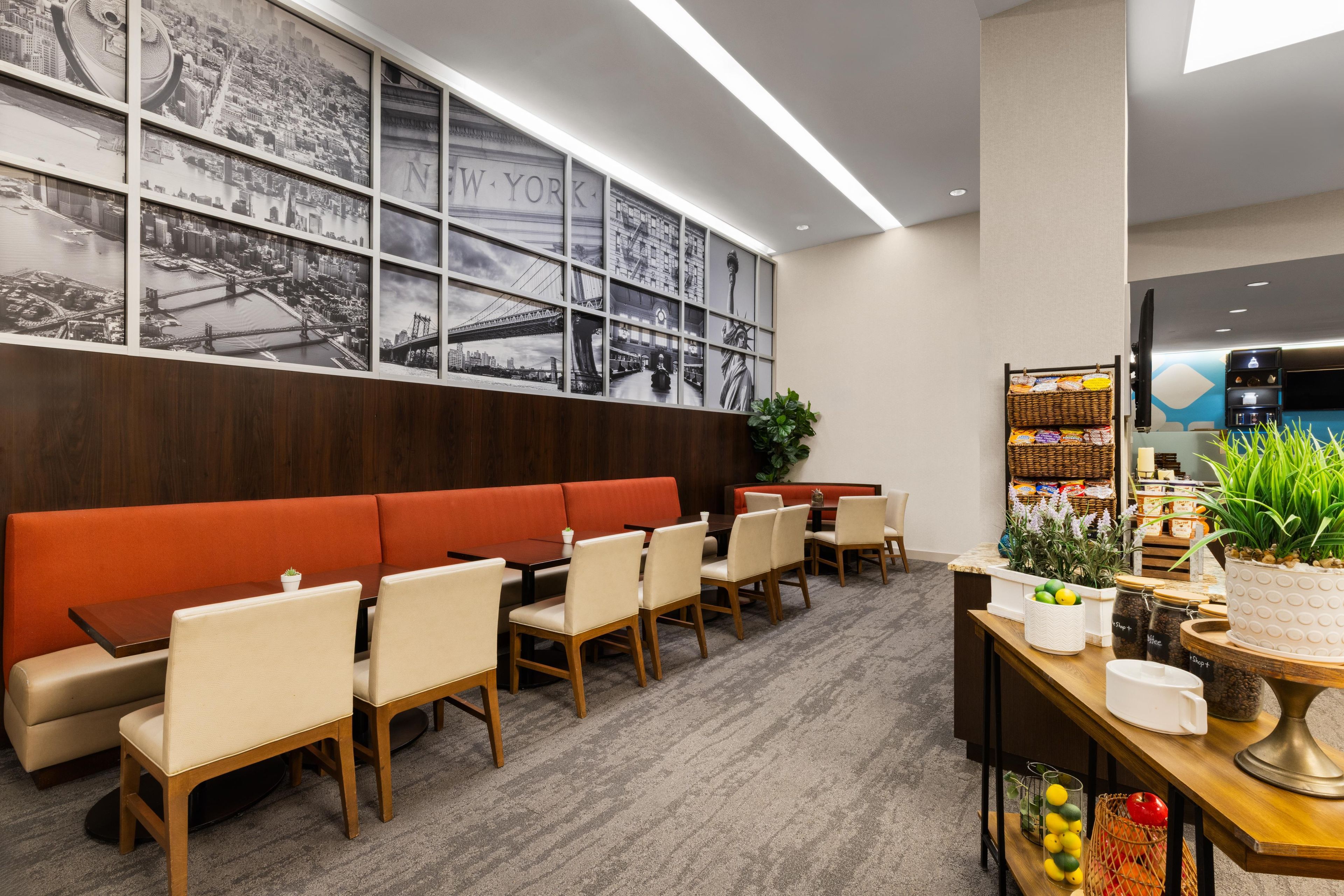 A hotel lobby with a red sofa, dining tables, chairs, a wall with black and white cityscape photos, and a television.