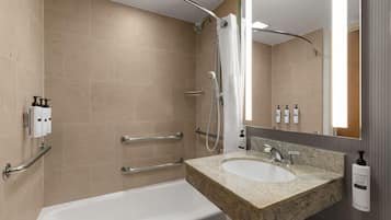 A modern bathroom with a bathtub, a sink with a granite countertop, and a shower area.