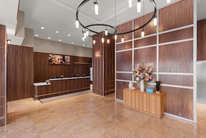 Un hall d’accueil d’hôtel avec un comptoir de réception en bois, un grand arrangement floral et un luminaire moderne.