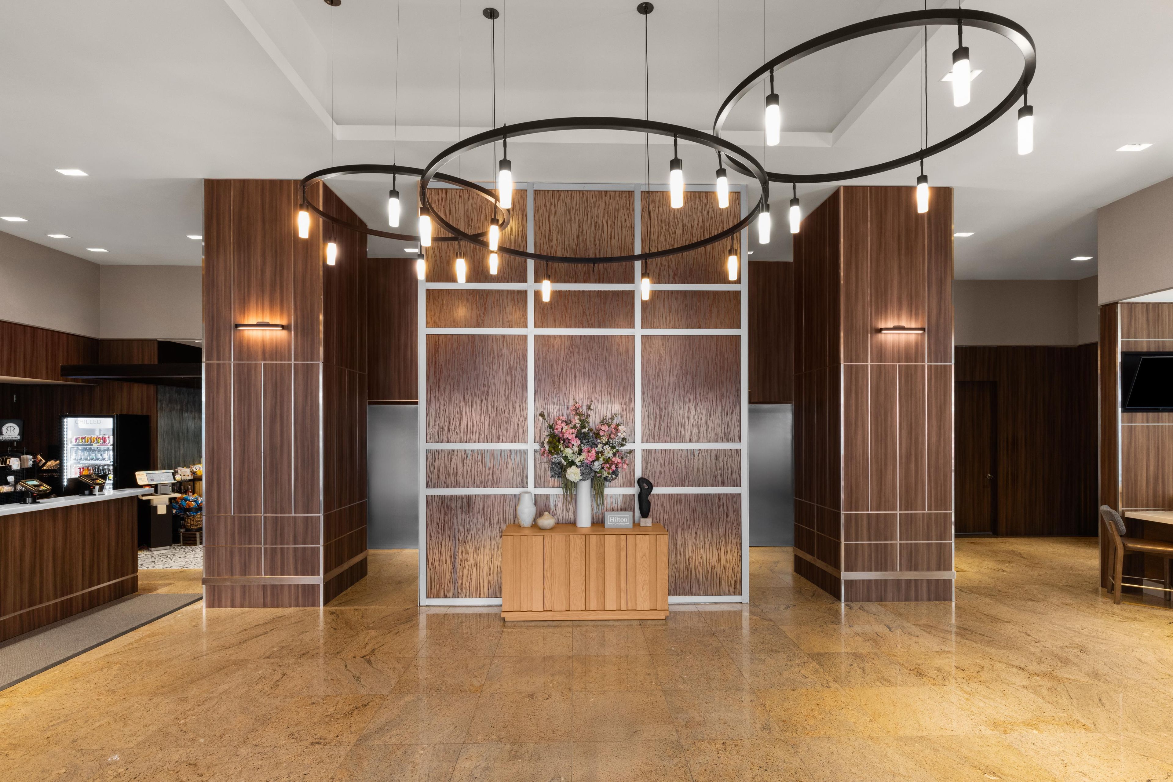 A hotel lobby with a reception desk, a floral centerpiece, and a modern light fixture.