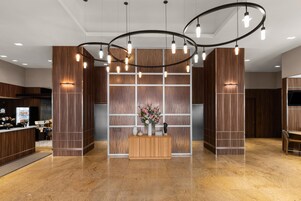 A hotel lobby with a reception desk, a floral centerpiece, and a modern light fixture.