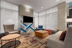 Un hall d’hôtel moderne doté d’un espace salon, d’un téléviseur à écran plat fixé au mur et de grandes fenêtres.
