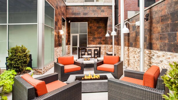 Un espace extérieur aménagé en terrasse, avec des meubles en osier, des coussins orange et un foyer central.