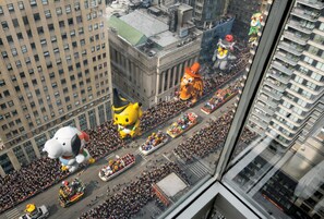 Un immeuble de grande hauteur offrant une vue sur un défilé de rue où l’on peut admirer de grands ballons en forme de personnages.
