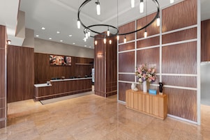 Een hotel receptie met een houten balie, een groot bloemstuk en een moderne lamp.