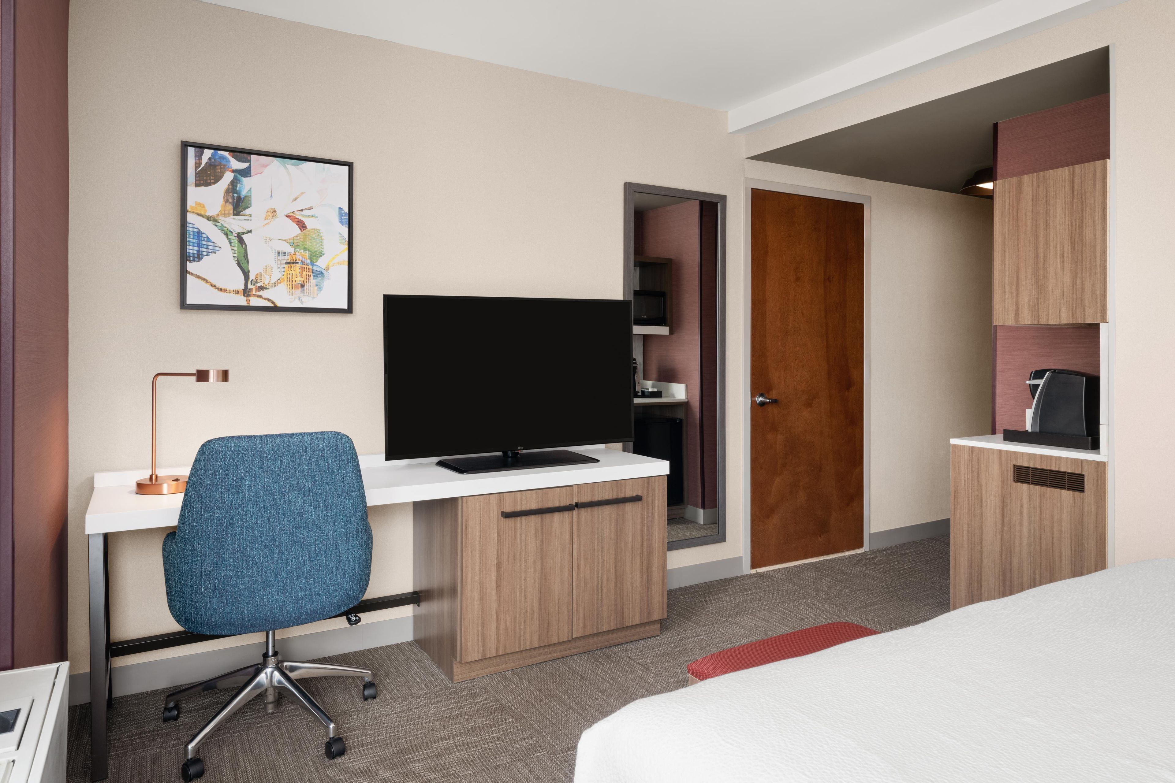 A hotel room with a bed, a desk with a computer, a chair, a television, and a door leading to a bathroom.