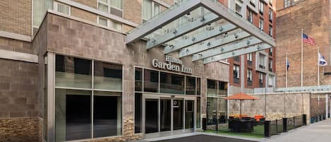 A Hilton Garden Inn with a modern entrance, large windows, and a covered outdoor area with seating.