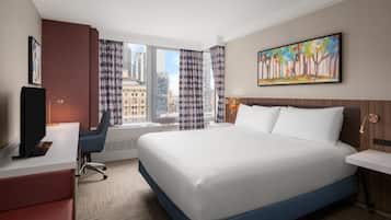 A hotel room with a large bed, a desk with a chair, a television, and a window with curtains.