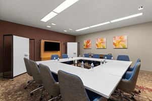 Uma sala de conferências com uma mesa comprida, cadeiras azuis e garrafas de água.