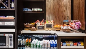 Un espace bar avec des étagères remplies d’en-cas, un réfrigérateur bien garni de boissons et un four à micro-ondes.