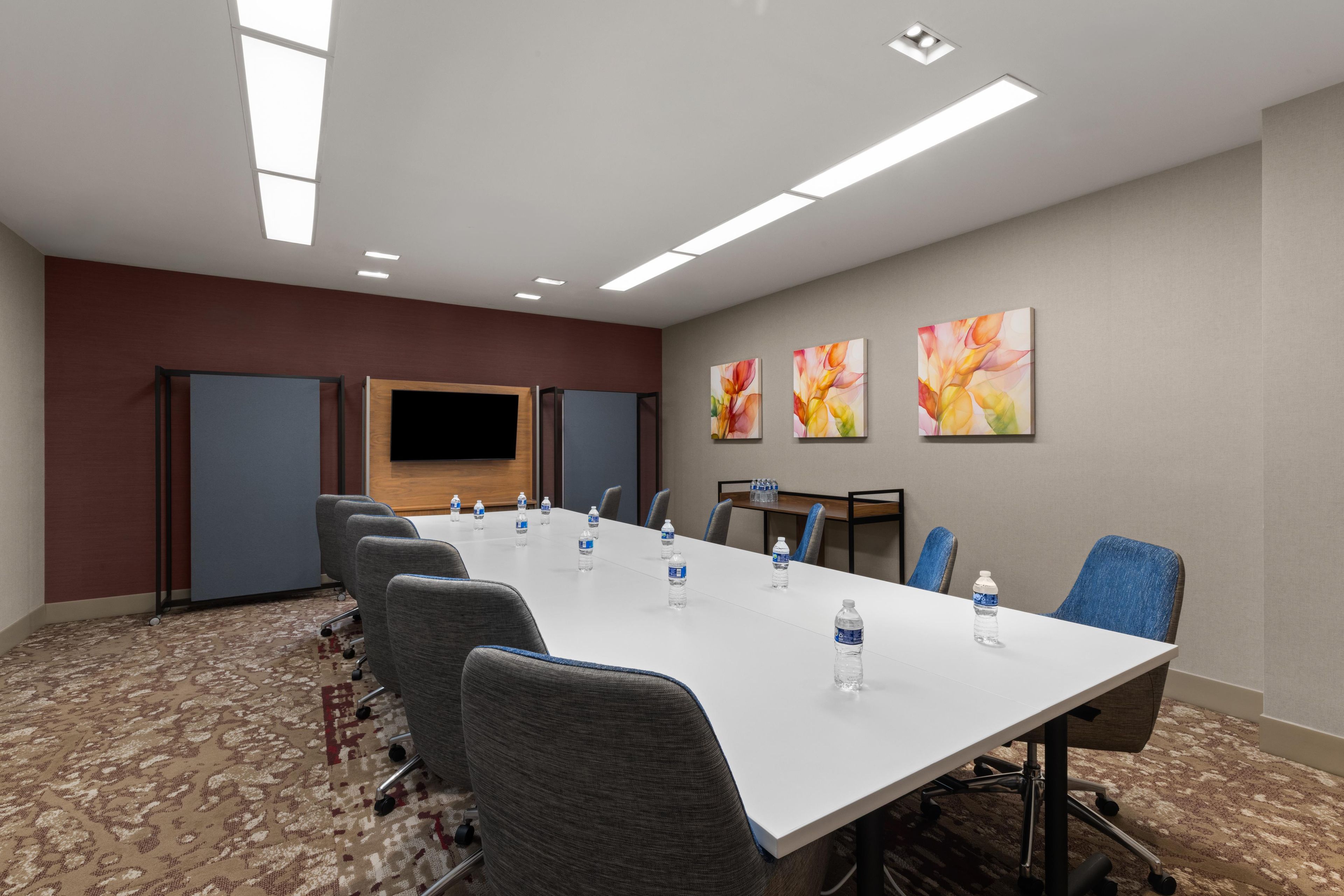 A conference room with a long table, chairs, a flat-screen TV, and artwork on the walls.