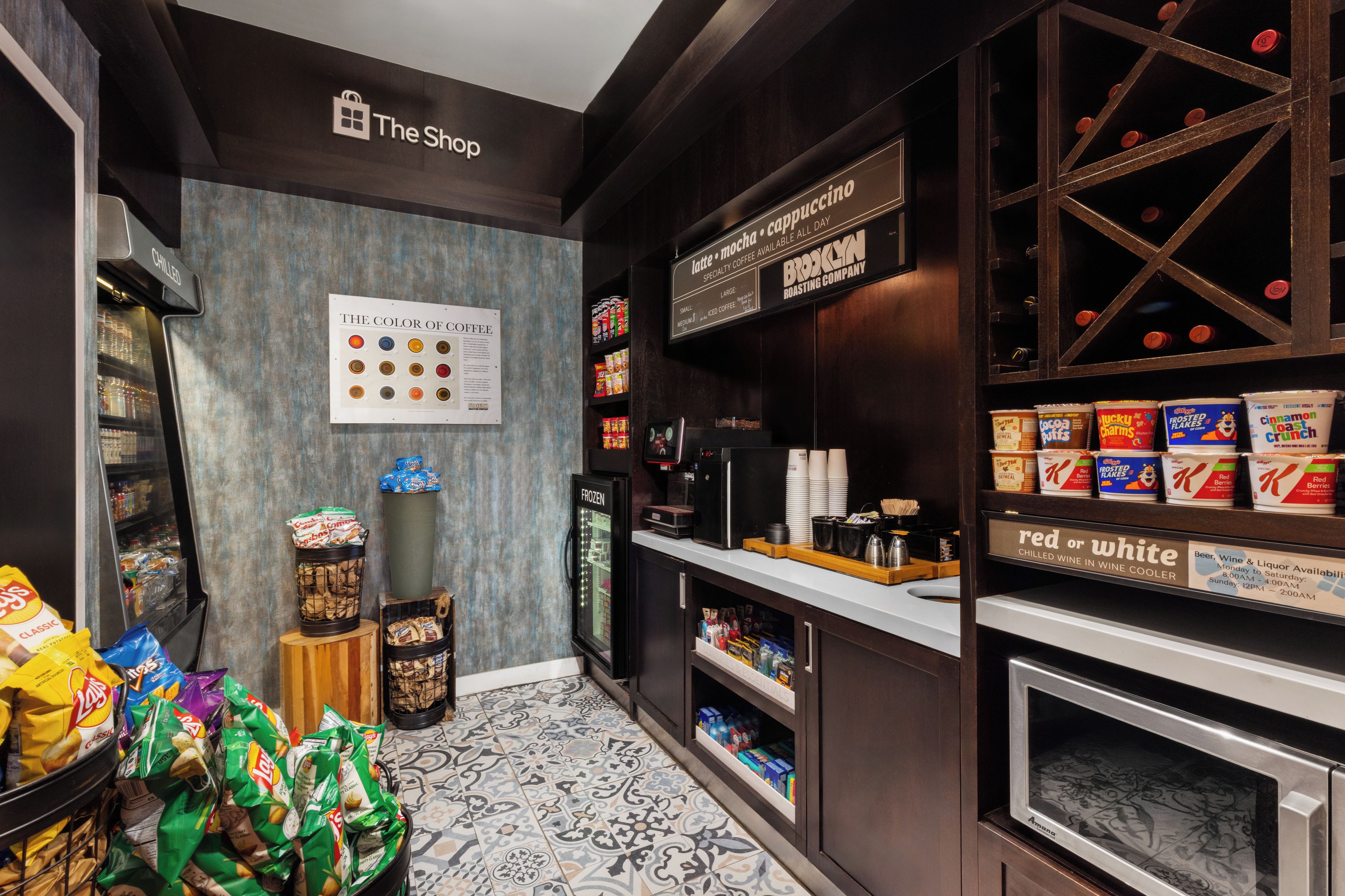 Interior de una cafetería con una máquina de café, una vitrina de aperitivos y un cartel que indica los tipos de café.