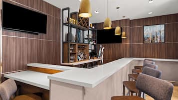 Un área de bar moderna con mostrador blanco, taburetes y una estantería para vinos.