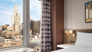 Une chambre d’hôtel avec une grande fenêtre, un lit, une table de chevet et une lampe fixée au mur.