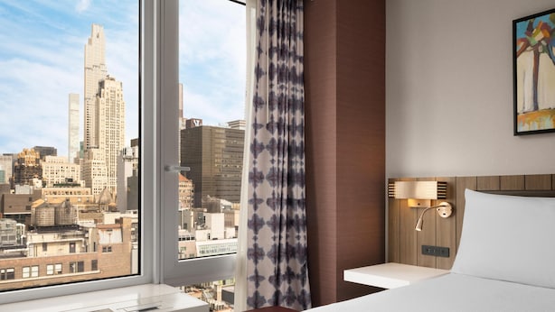 Hotelkamer met een groot raam, een bed, een nachtkastje en een wandlamp.