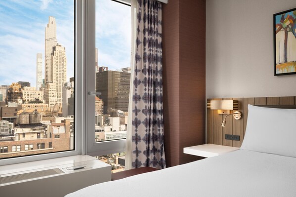 Une chambre d’hôtel avec une grande fenêtre, un lit, une table de chevet et une lampe fixée au mur.