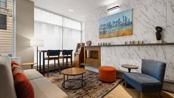 A modern living room with a sofa, chairs, a coffee table, a fireplace, and a cityscape painting on the wall.