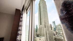 Une vue sur l’Empire State Building, prise depuis une fenêtre avec un rideau.